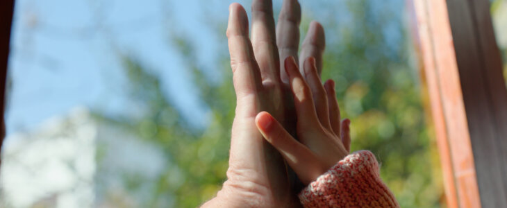 Child, parent and hands on glass by window in home for separation, game or barrier to connection. People, kid and palm with touch for bonding, love and care in morning for development at family house