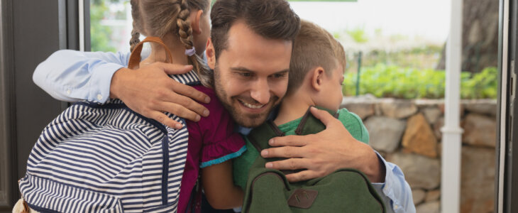 Front view of Caucasian father embracing his children at door in a comfortable home