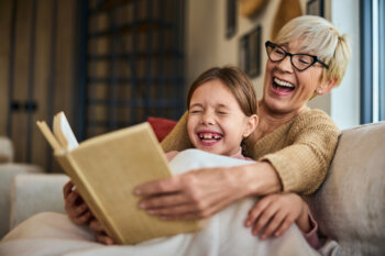 Grandchild and her grandma laughing while reading a book together.