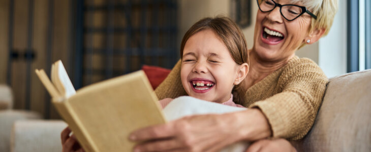 Grandchild and her grandma laughing while reading a book together.