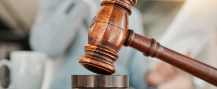 Closeup, gavel and law on table, office and attorney man in blurred background with phone call for networking. Advocate, lawyer or judge with legal hammer, paperwork or documents for court evidence