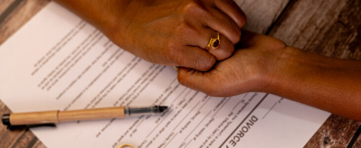 Holding hands for support during divorce proceedings. Wedding rings and agreement on table.